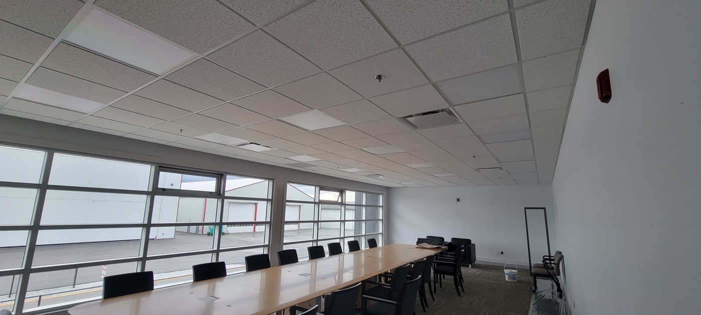 Completed suspended T-bar ceiling with white acoustic tiles and integrated lighting in a commercial room. Completed suspended T-bar ceiling with white acoustic tiles and integrated lighting in a commercial room.